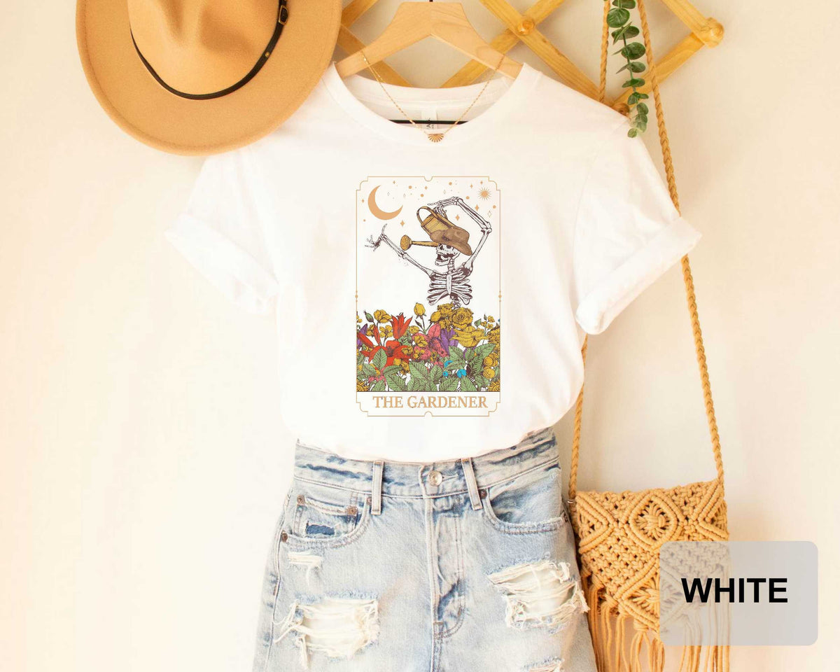 a white t-shirt with a graphic design of a skeleton holding a flower, along with a pair of denim shorts and a beige hat.