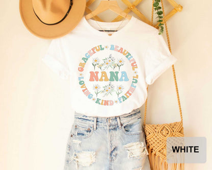 A white t-shirt with a colorful floral design and the text "NANA" printed on it, along with a pair of distressed denim shorts and a straw hat.