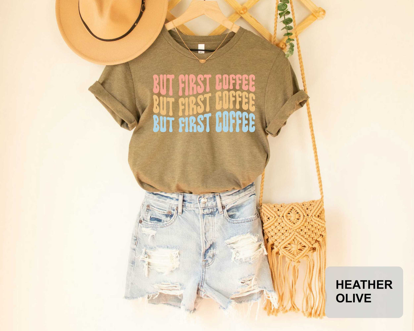 A casual outfit consisting of a t-shirt with a text design, denim shorts, and a straw bag is displayed on a hanger against a white wall.