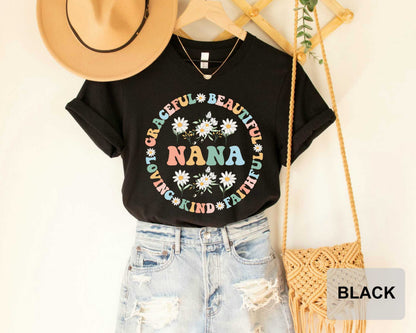 A black t-shirt with a colorful floral design, a beige hat, a pair of distressed denim shorts, and a woven purse are displayed in the image.